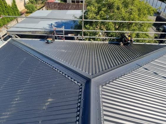 Fresh dark corrugate hip roof with a roofer working