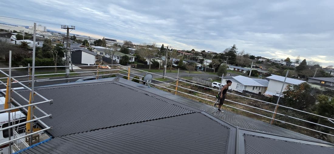 Roofer on a new dark long-run roof overlooking Hamilton